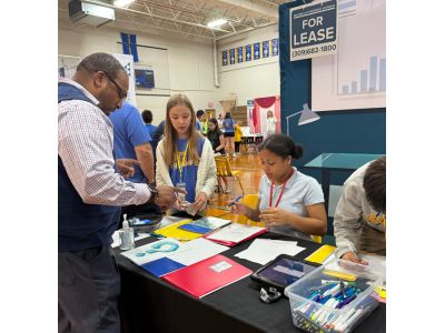 Photo of a volunteer helping students behind a table run a storefront in JA BizTown Mobile