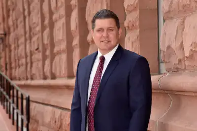 Sid Ruckriegel wearing a suit and smiling in front of a stone building