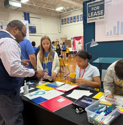 Photo of a volunteer helping students behind a table run a storefront in JA BizTown Mobile